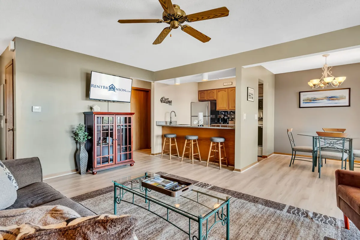 An open-concept interior that seamlessly connects the living area, dining table, and kitchen bar counter. The arrangement invites relaxation and socializing, with a large TV positioned for movie nights and ample seating for guests.