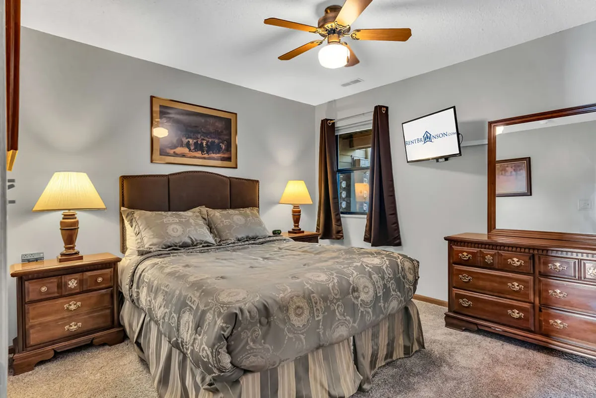 A sunlit bedroom with a comfortable bed, nightstand, dresser, and window, all accented with stylish artwork. The overall ambiance feels tranquil and homey, ideal for guests seeking relaxation after a day of adventure.