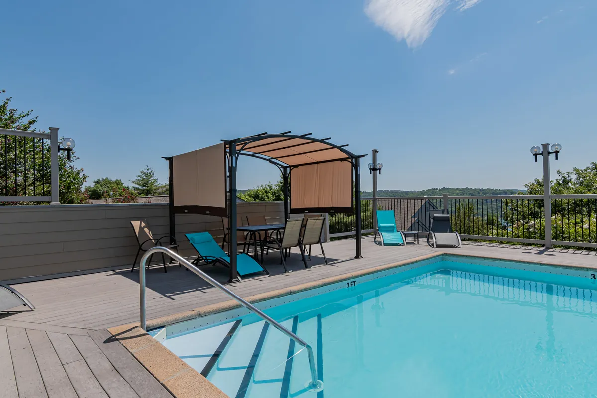 An inviting outdoor swimming pool framed by lounge chairs and a canopy seating area, all set against a backdrop of lush greenery and distant hills. The space exudes relaxation and is ideal for family fun and unwinding after a day of adventure.