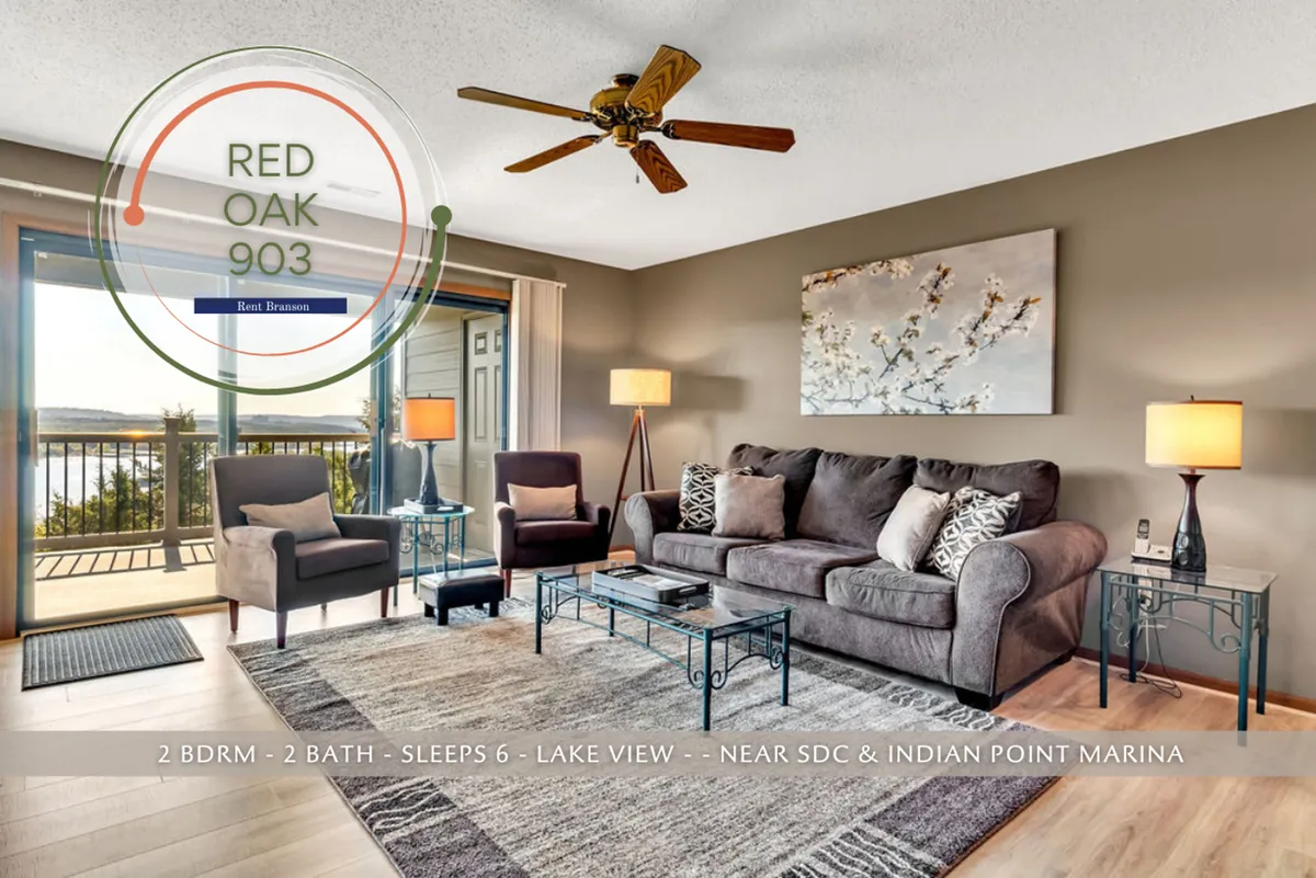 A cozy, open living room featuring a comfortable seating arrangement, decorative artwork on the wall, and expansive windows that showcase a breathtaking view of the lake. The room is filled with natural light, creating a warm and inviting atmosphere perfect for family gatherings and movie nights.