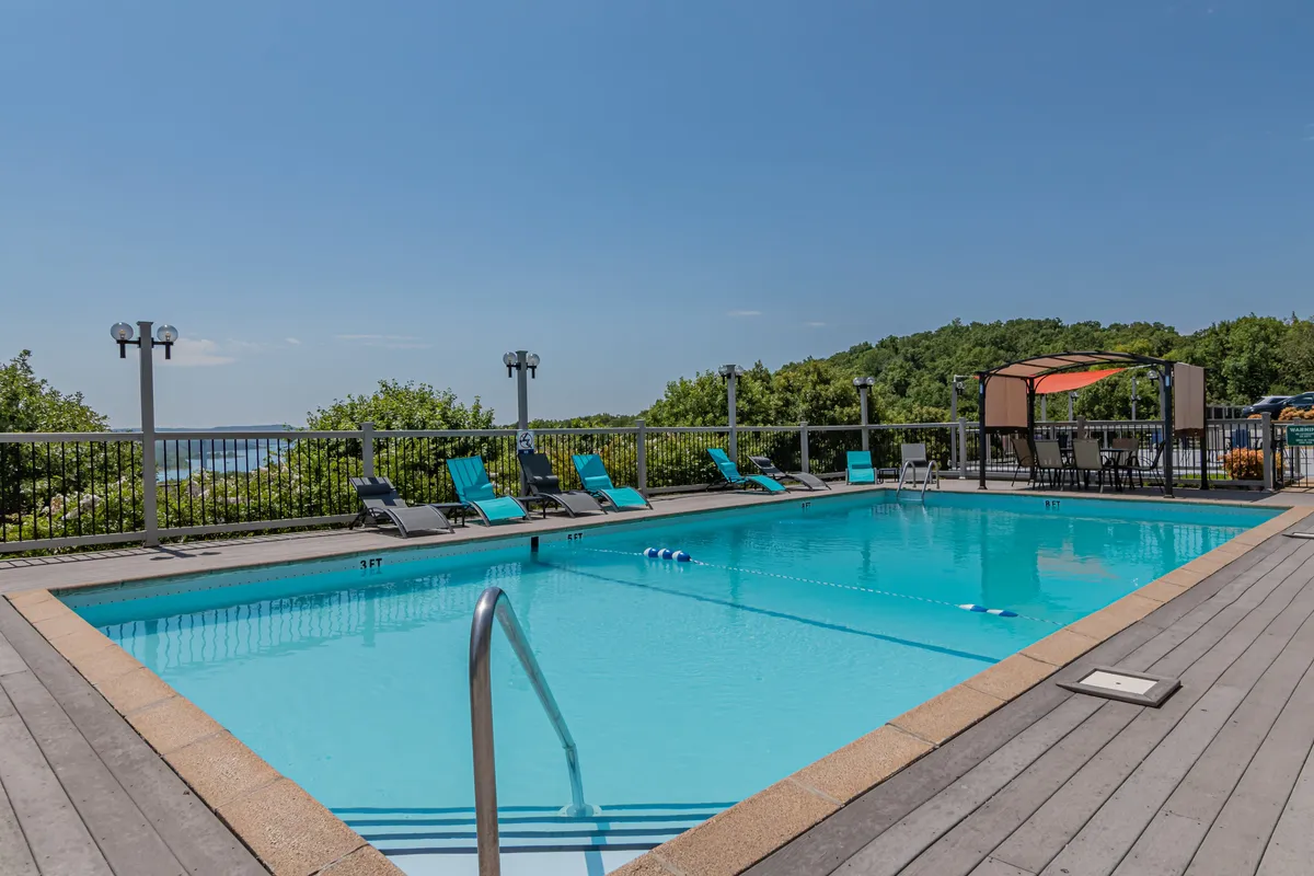 A beautifully maintained outdoor swimming pool surrounded by lounge chairs, a canopy for shade, and lush greenery. The scene feels tranquil and inviting, ideal for relaxation or social gatherings during the warmer months.