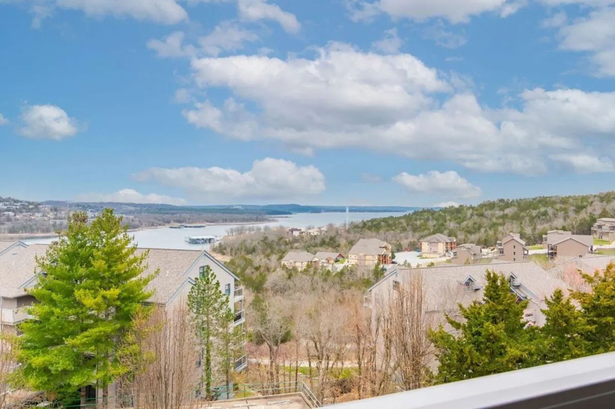 A tranquil view of Table Rock Lake with gentle waves, distant wooded hills, and a cluster of residential buildings dotting the shoreline under a cloudy sky. The natural setting evokes outdoor adventure and peaceful family moments by the water.