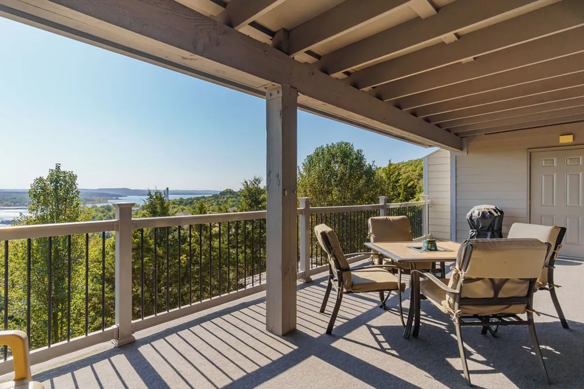 The image showcases an inviting outdoor dining table set on a spacious deck, surrounded by lush greenery and overlooking a stunning, tranquil view of Table Rock Lake. The scene is bathed in soft, natural light, evoking a peaceful atmosphere perfect for both sunrise breakfasts and evening gatherings under the stars.