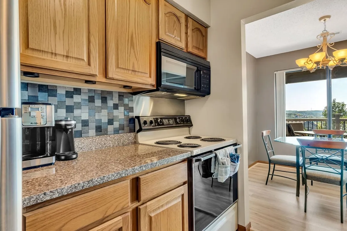 A welcoming kitchen with modern appliances, granite countertops, and a decorative backsplash. The kitchen opens to a dining area with large windows that frame a tranquil lake view, blending culinary space with scenic beauty.